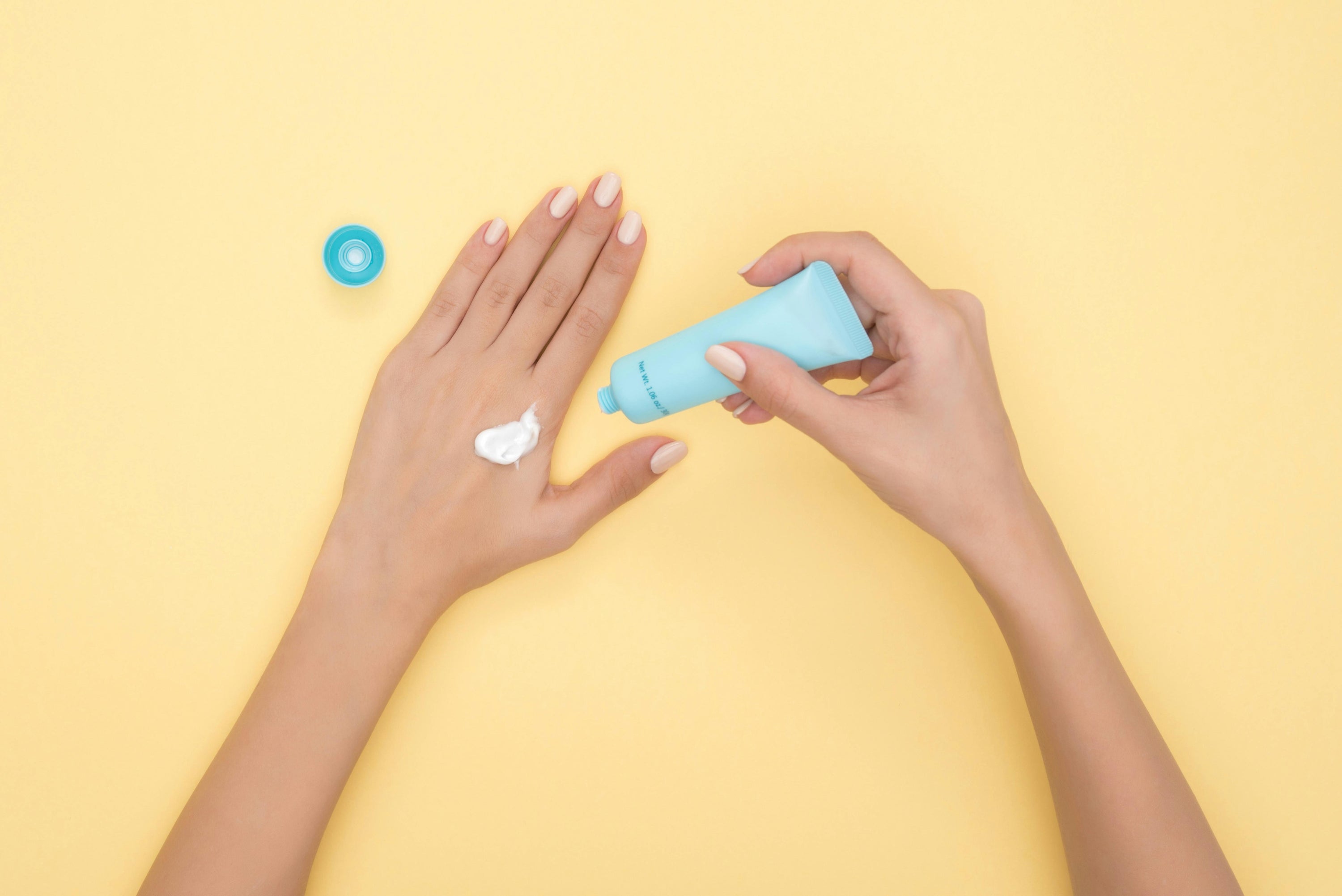 Hands applying sunscreen from blue bottle with yellow background